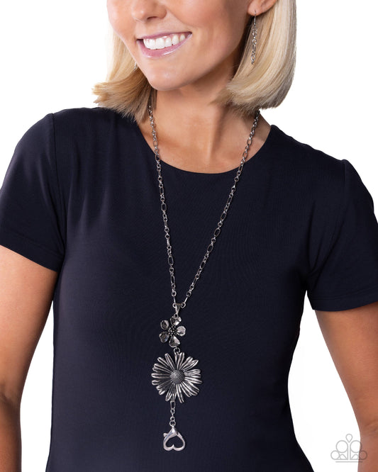 Woman wearing a long silver necklace with floral pendants on a white background