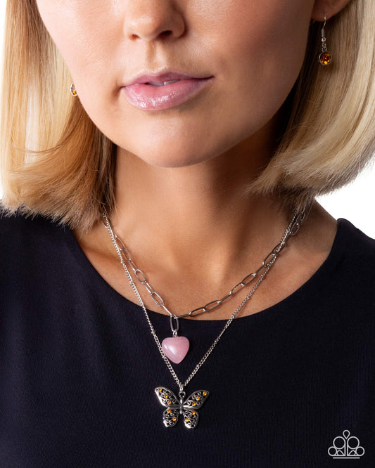 Close-up of a woman wearing a butterfly pendant necklace on a plain background