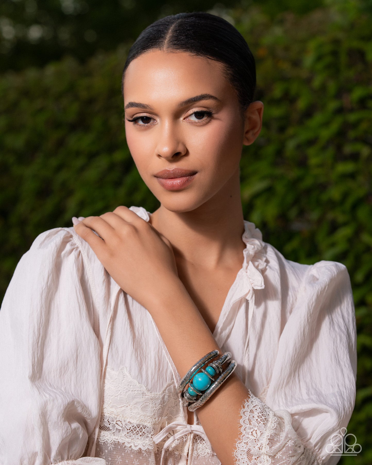 Woman wearing a white blouse with turquoise bracelet against a green background