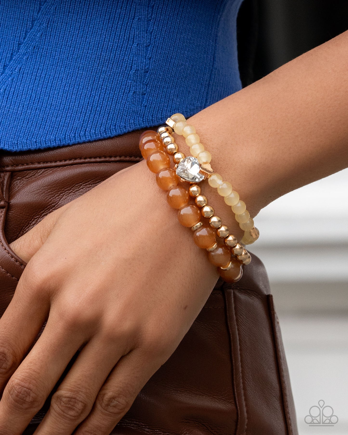 Close-up of a wrist wearing multiple beaded bracelets with a blue top and brown leather jacket.