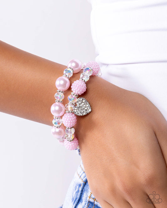 Pink beaded bracelet with heart charm on a wrist against a white background