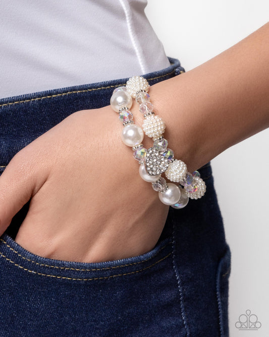 Close-up of a hand wearing a pearl and crystal bracelet on a plain background
