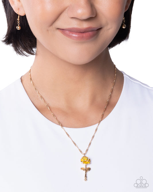 Person wearing a rose gold necklace with a yellow pendant on a white background