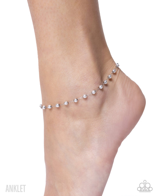 Silver anklet on a foot against a white background