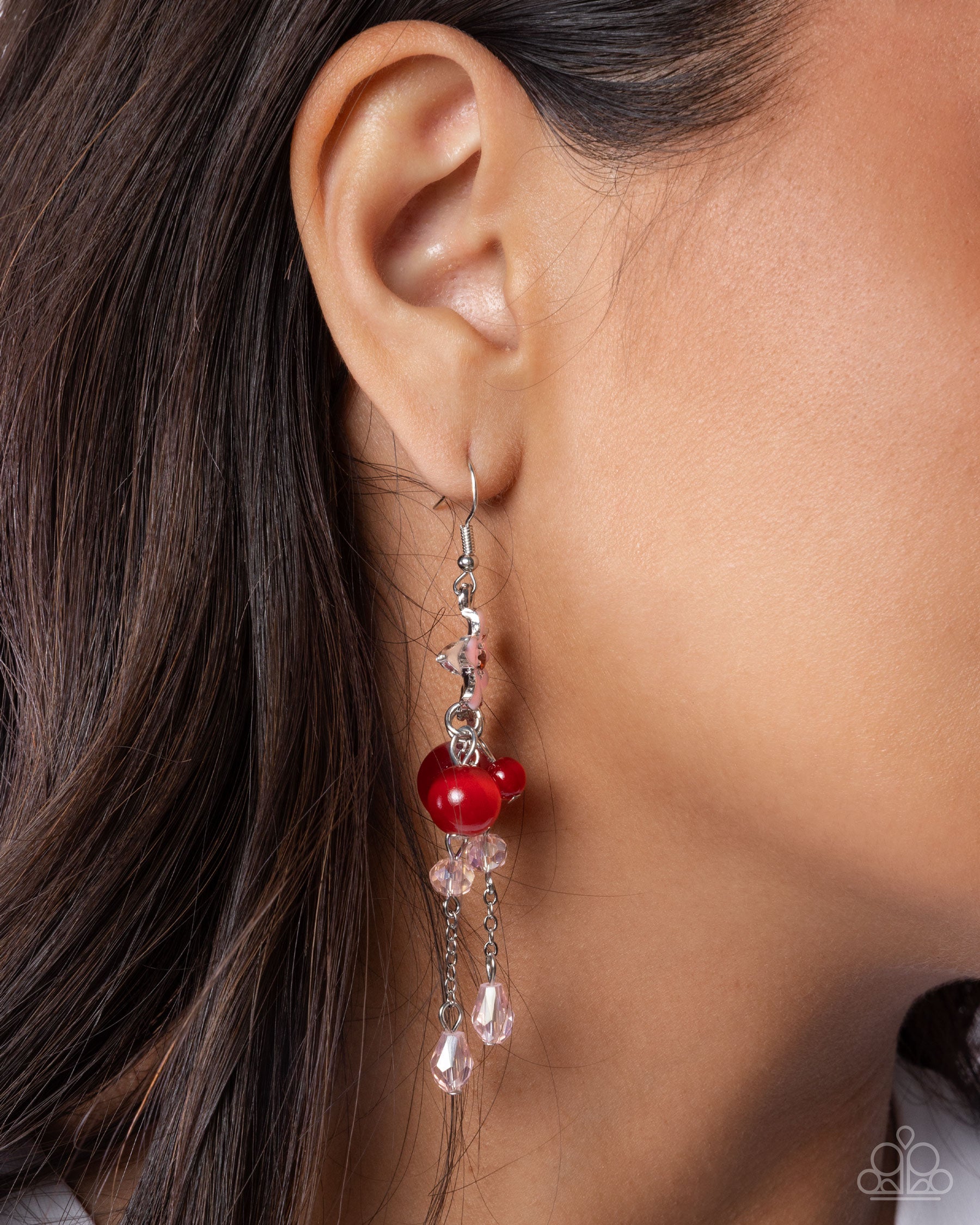 Close-up of an ear wearing a red berry earring with dangling crystals.