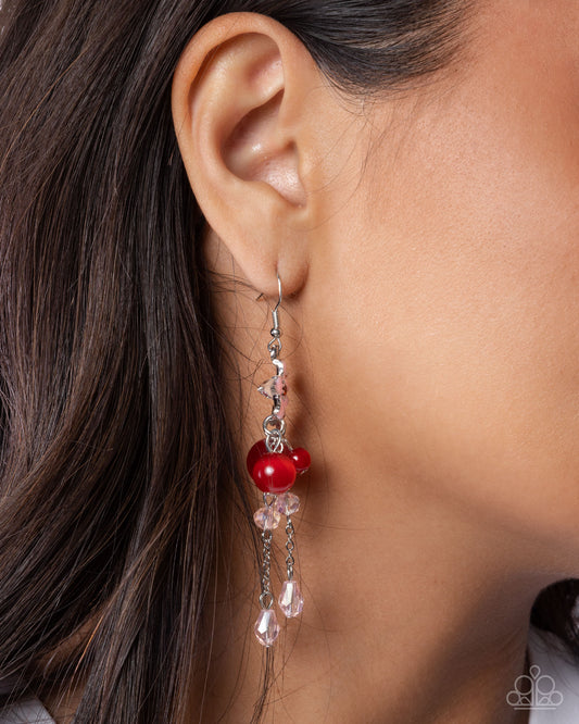Close-up of an ear wearing a red berry earring with dangling crystals.