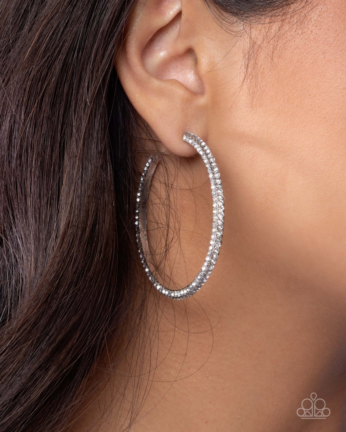 Silver hoop earring worn by a person with dark hair.