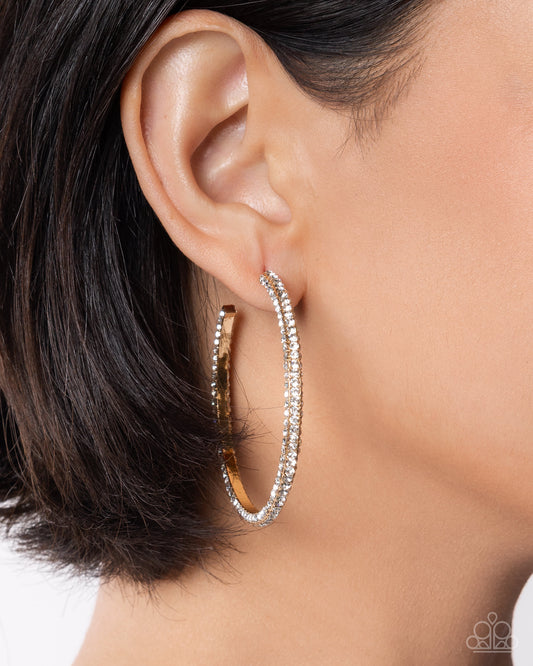 Close-up of an ear wearing a silver hoop earring with clear stones on a neutral background