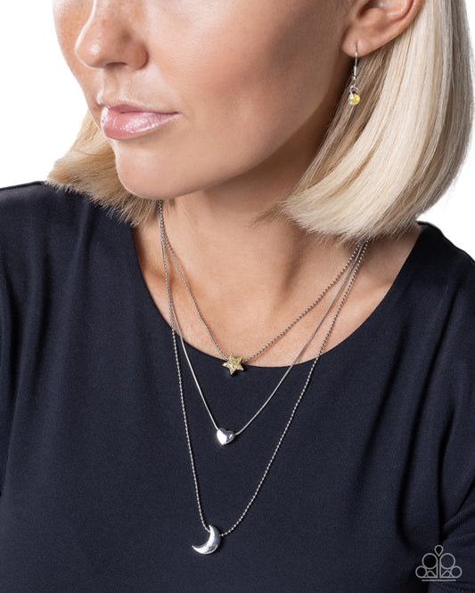 Close-up of a woman wearing a silver necklace with star and moon pendants on a plain background