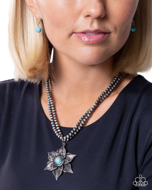 Woman wearing a beaded necklace with a silver flower pendant and turquoise stones.