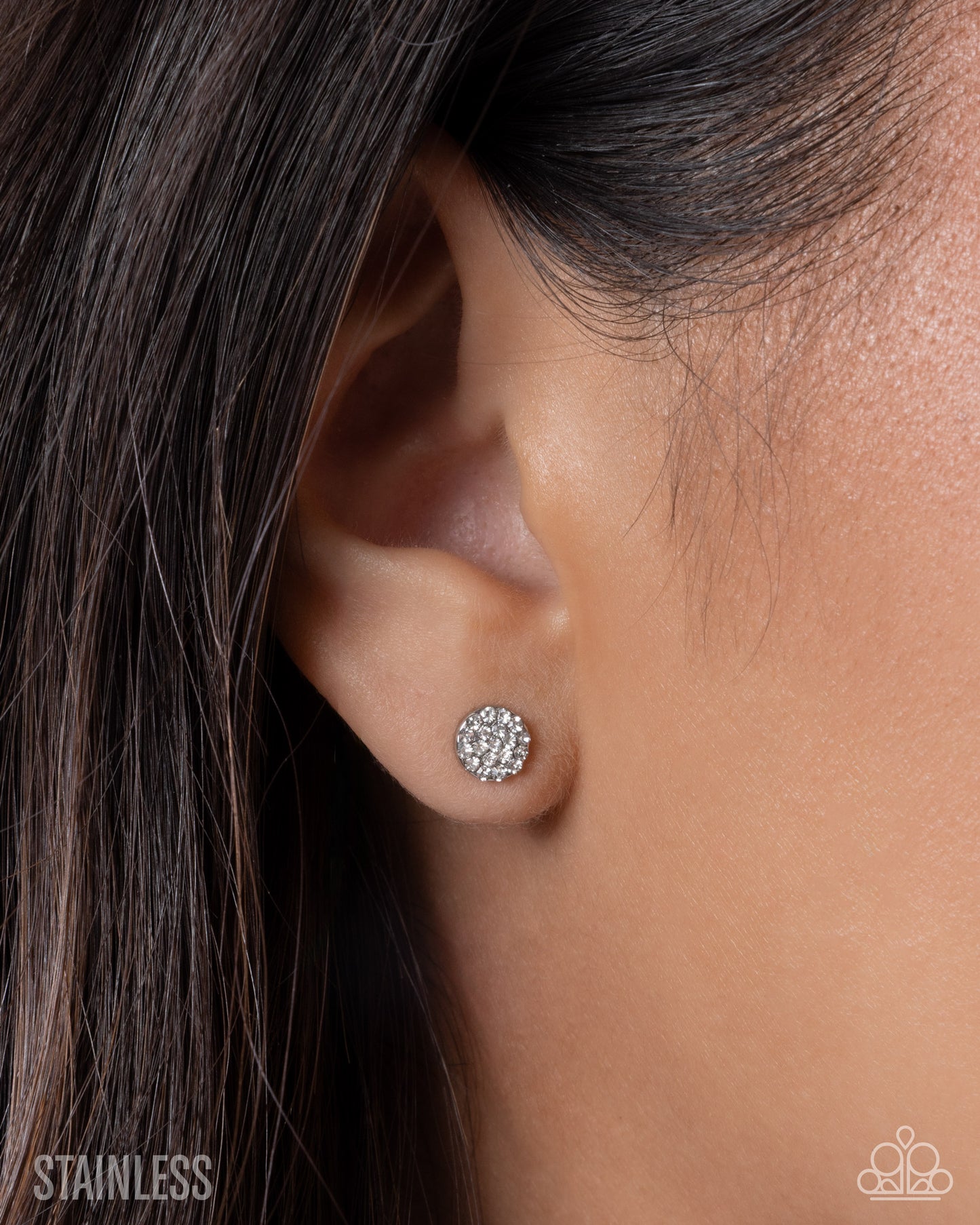 Close-up of an ear wearing a silver earring with 'Stainless' text below.