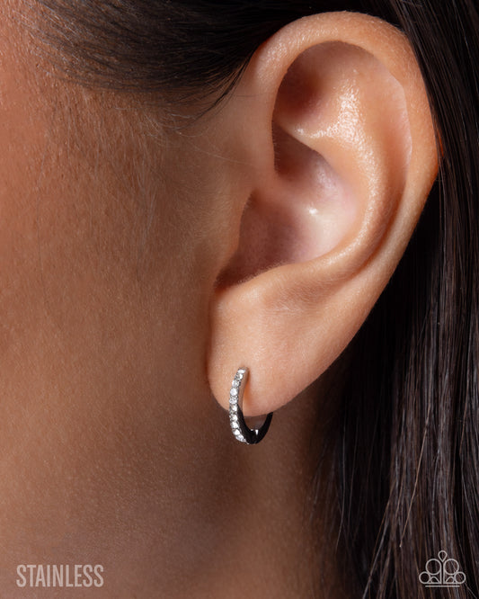 Close-up of an ear wearing a silver hoop earring with 'Stainless' text below.