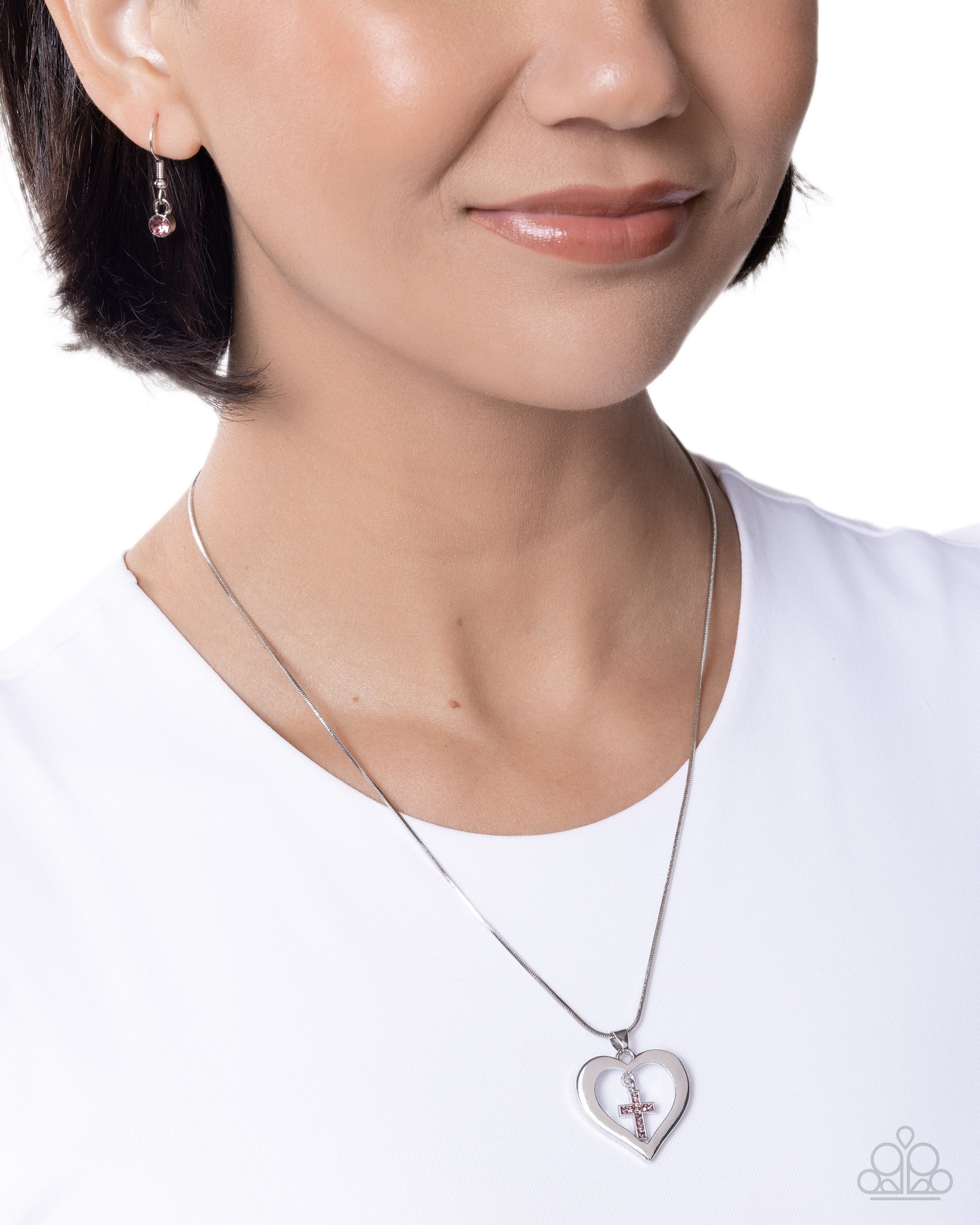 Person wearing a silver necklace with a heart-shaped pendant on a white background
