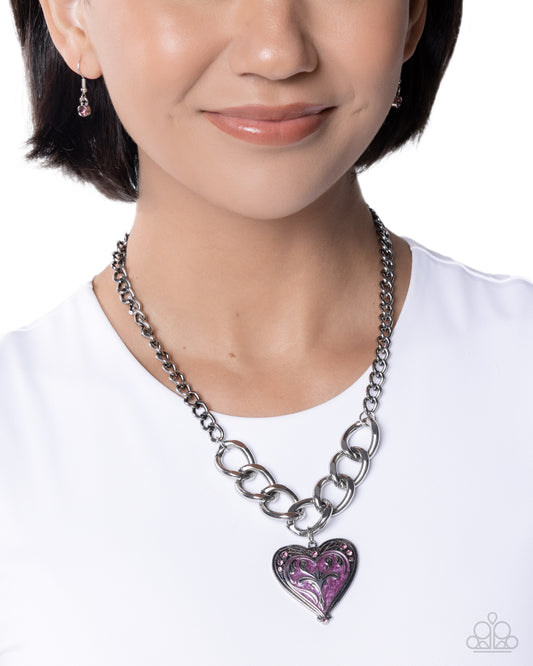 Person wearing a silver chain necklace with a purple heart pendant on a white background