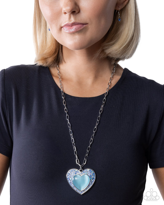 Woman wearing a black shirt with a blue heart-shaped pendant necklace on a white background