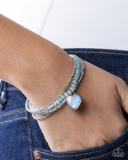 Stack of bracelets on a wrist with a heart-shaped opal stone against a denim background