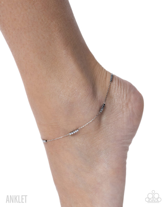 Silver anklet on a person's ankle against a white background