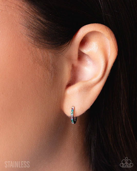 Close-up of an ear wearing a black and blue earring with 'Stainless' text.