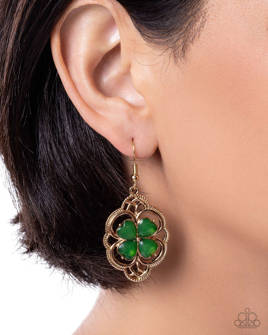 Gold earring with green clover design worn by a person