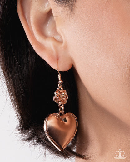 Rose gold heart-shaped earring worn by a person with dark hair.