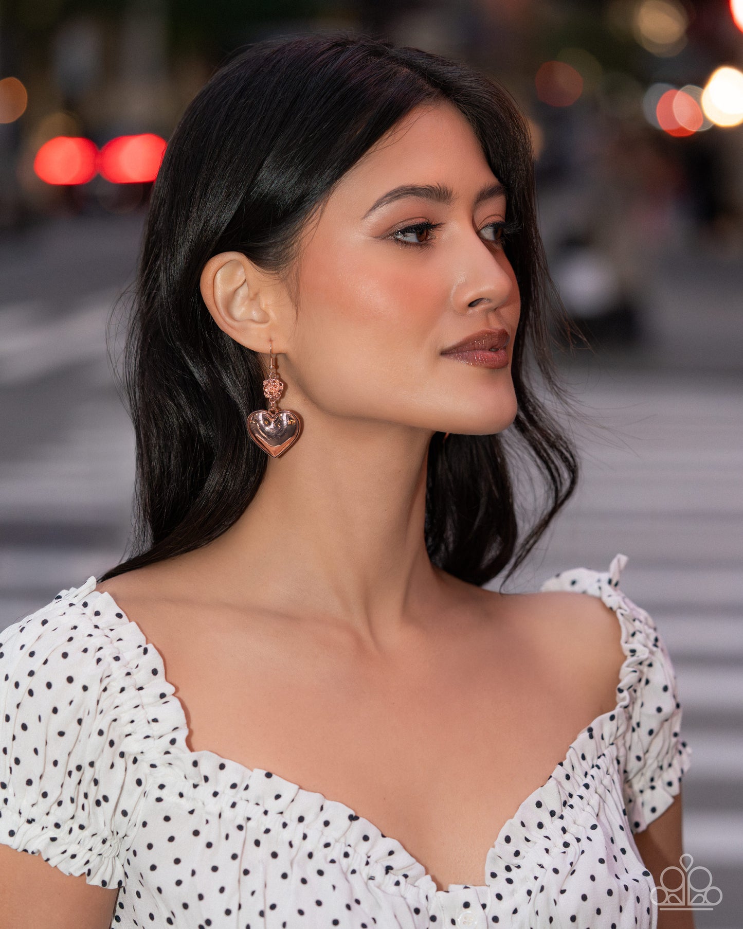 Woman wearing a white polka dot dress with a blurred city street background