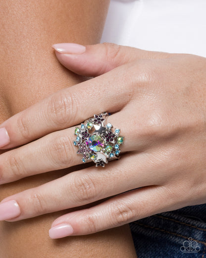Close-up of a hand wearing a decorative ring with multicolored gemstones.