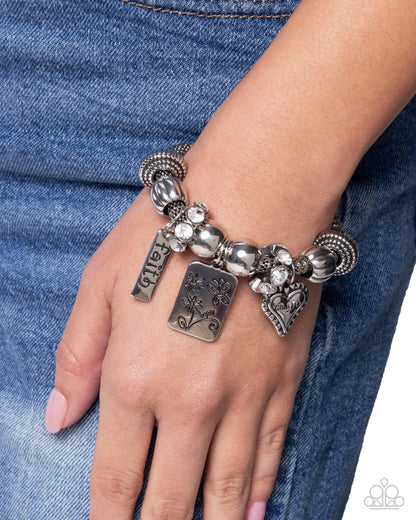 Silver bracelet with charms on a wrist against a denim background