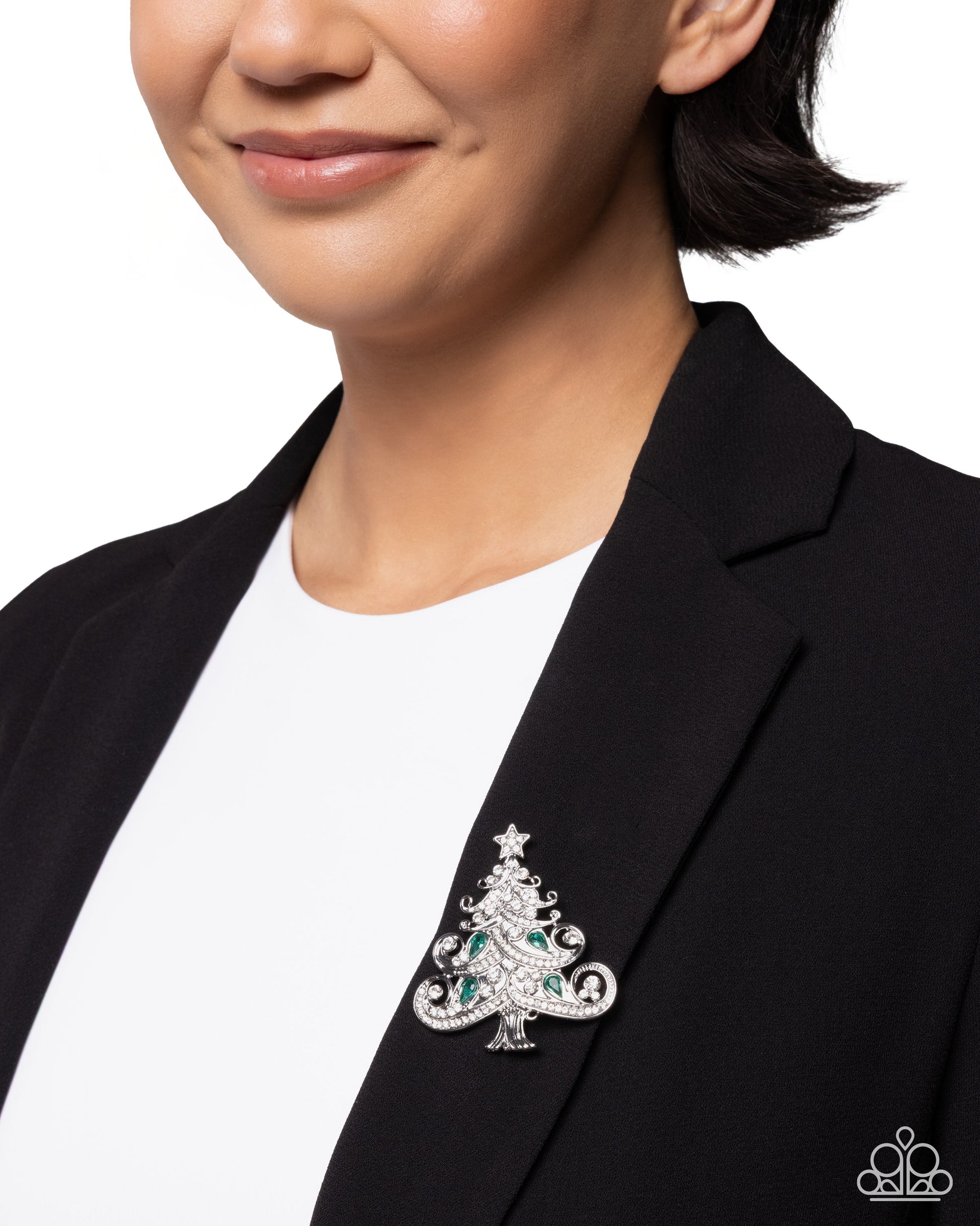 Person wearing a black blazer with a decorative Christmas tree brooch on a white background