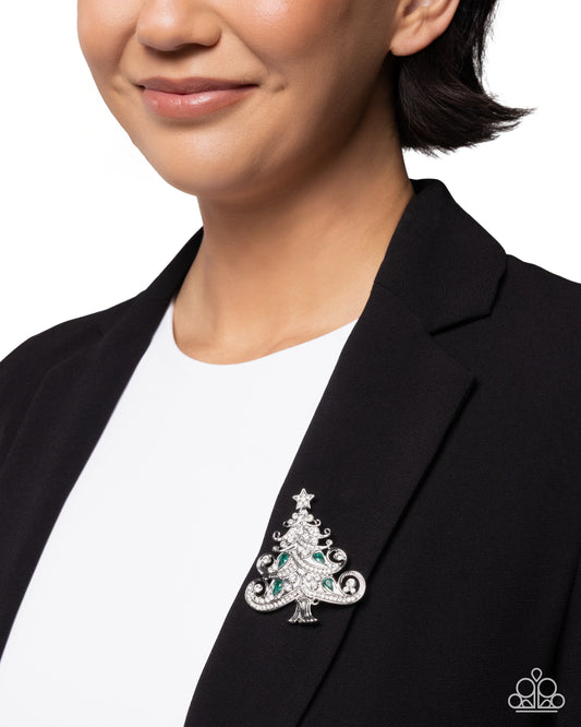 Person wearing a black blazer with a decorative Christmas tree brooch on a white background