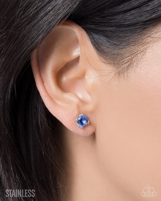 Close-up of an ear wearing a blue gemstone earring with 'Stainless' branding.