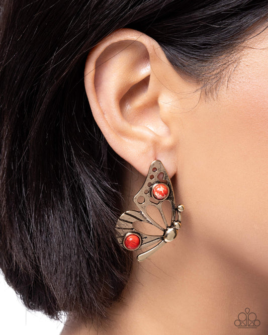 Butterfly-shaped earring with red stones worn by a person with dark hair.