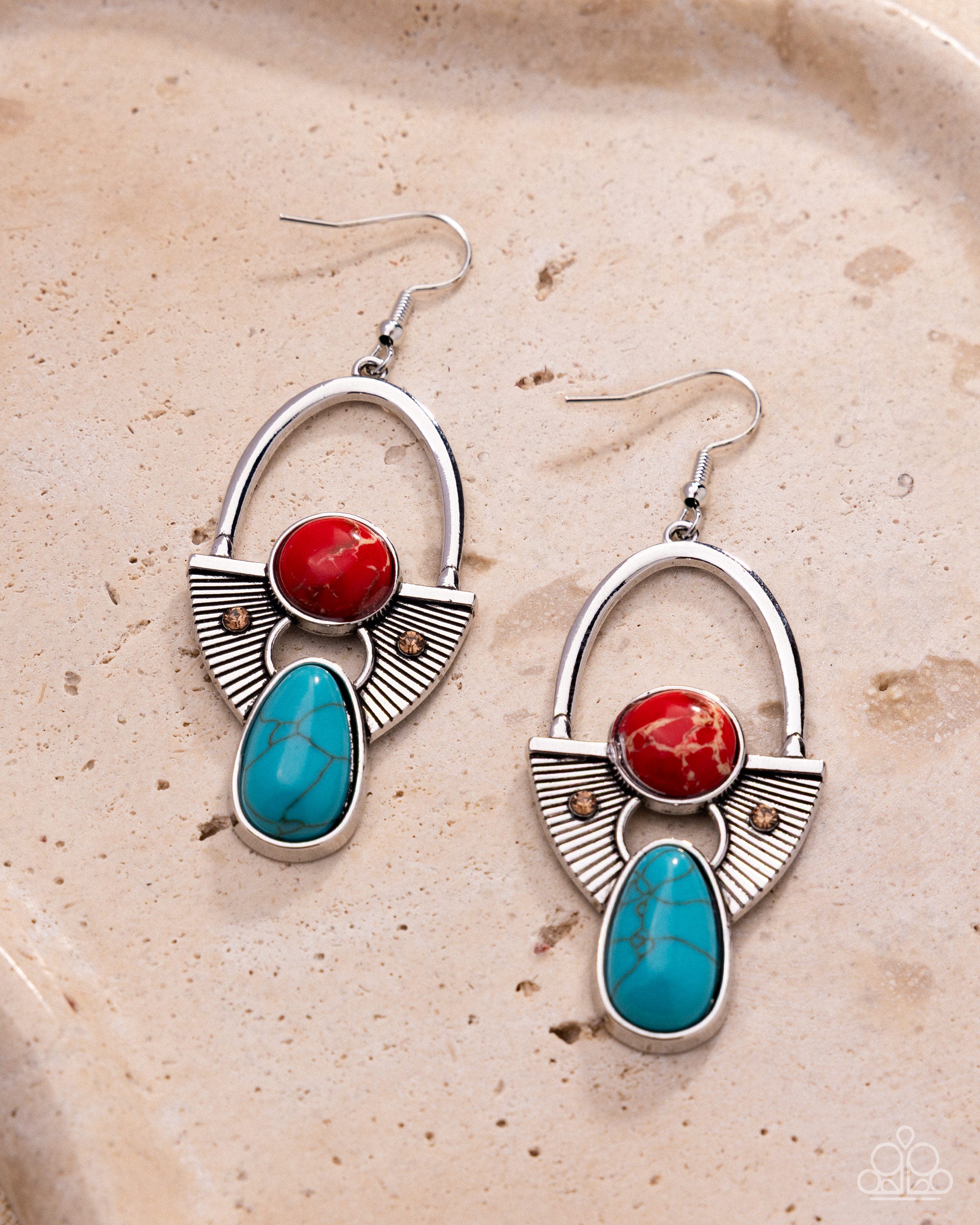 Pair of silver earrings with red and turquoise stones on a beige stone surface