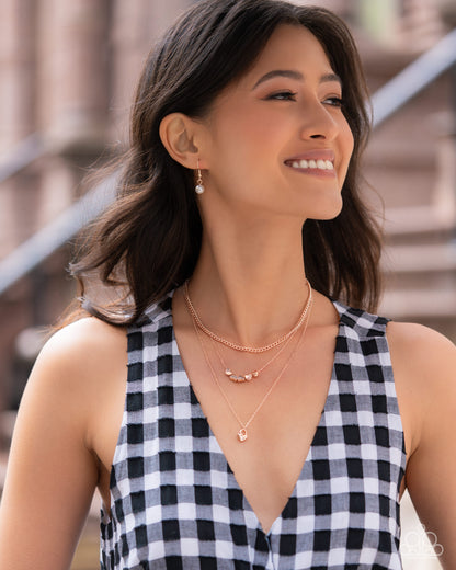 Woman wearing a black and white checkered dress with layered necklaces, smiling outdoors.