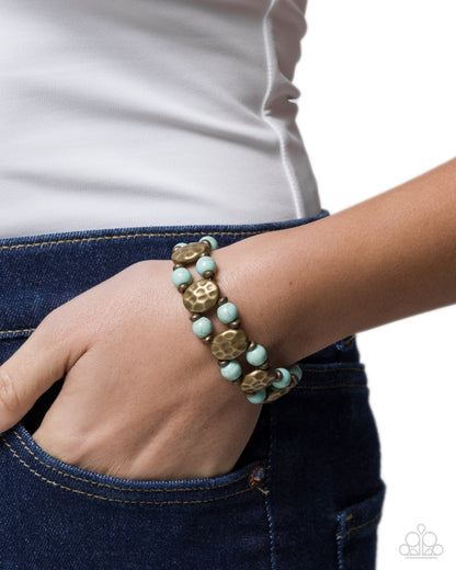 Turquoise and gold beaded bracelet on a wrist with a white background