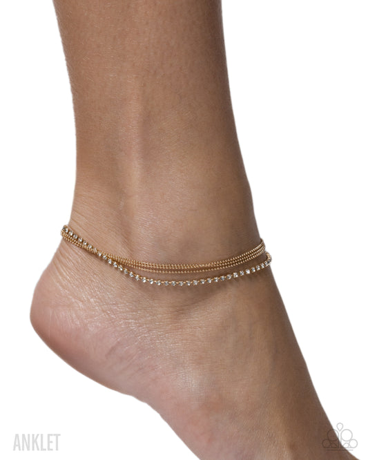 Gold anklet on a foot against a white background