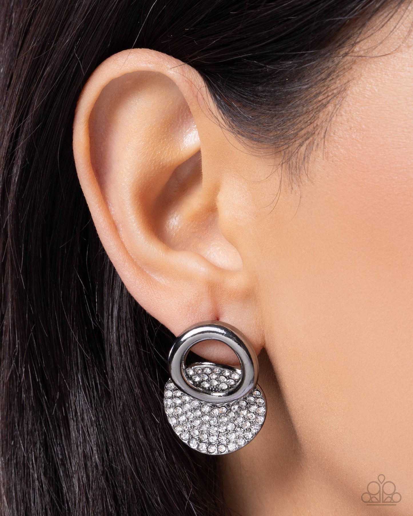 Close-up of an ear wearing a silver earring with a circular design.