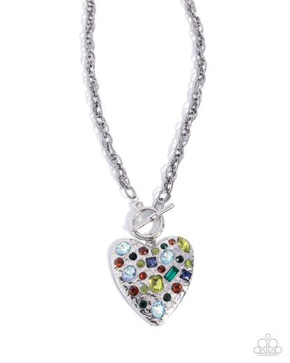 A silver heart-shaped pendant necklace adorned with multicolored rhinestones, suspended from a silver cable chain on a white background.