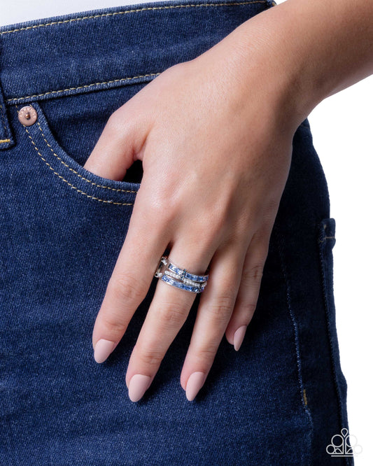 Hand wearing a stack of rings on a blue denim background