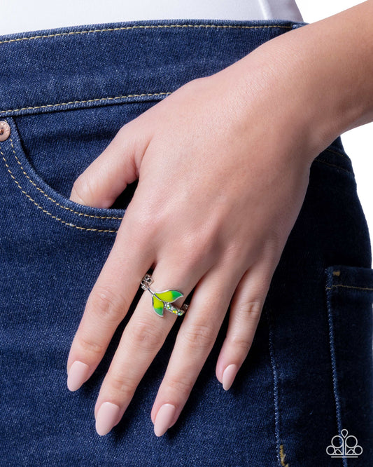 Hand wearing a green and silver ring on a blue denim background