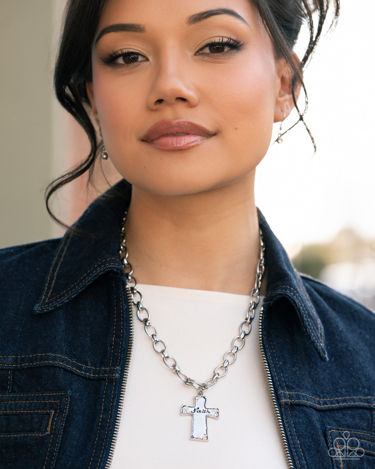 Woman wearing a silver necklace with a cross pendant, standing outdoors.