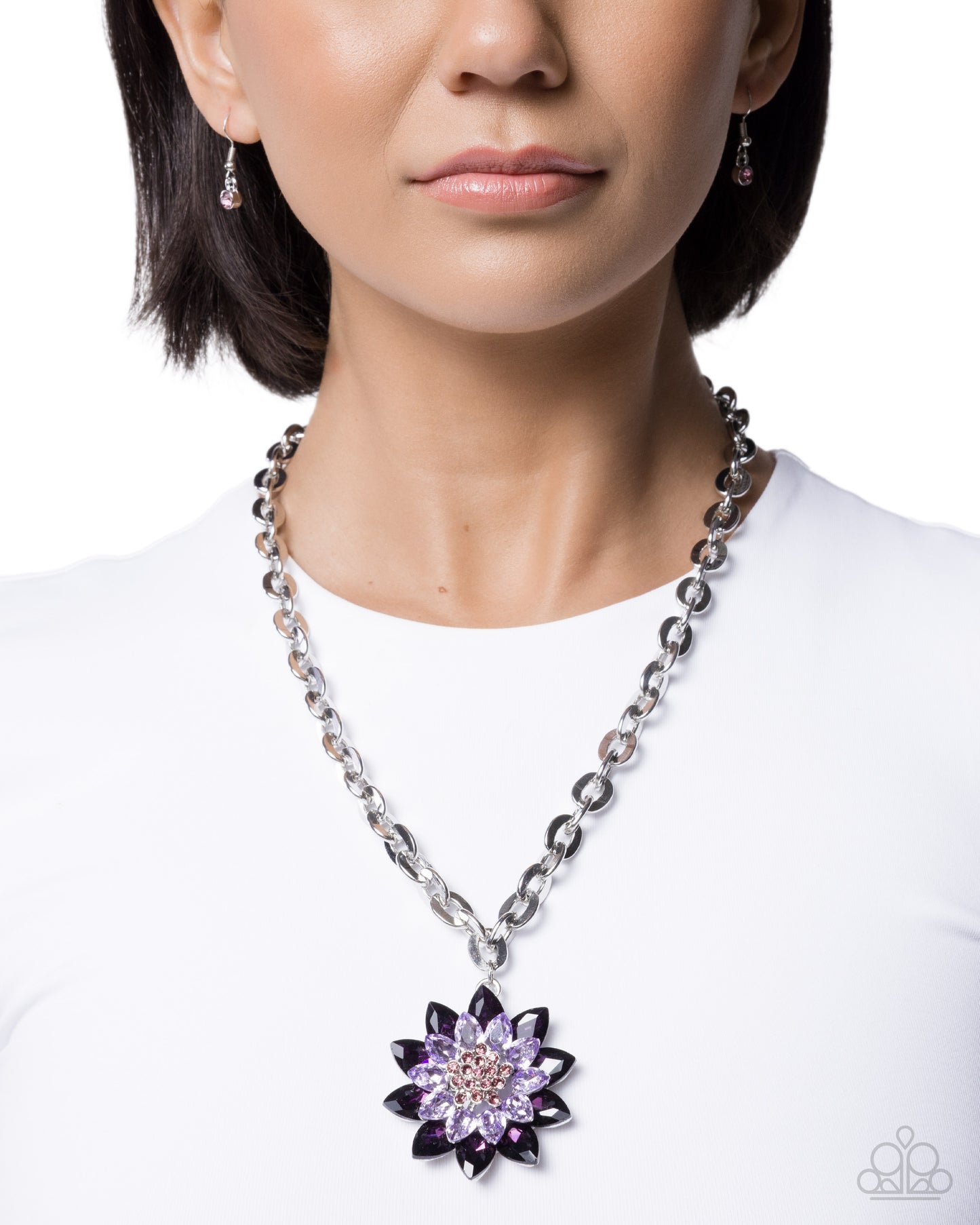 Person wearing a silver chain necklace with a purple flower pendant on a white background