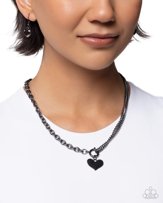 Person wearing a black chain necklace with a heart pendant on a white background