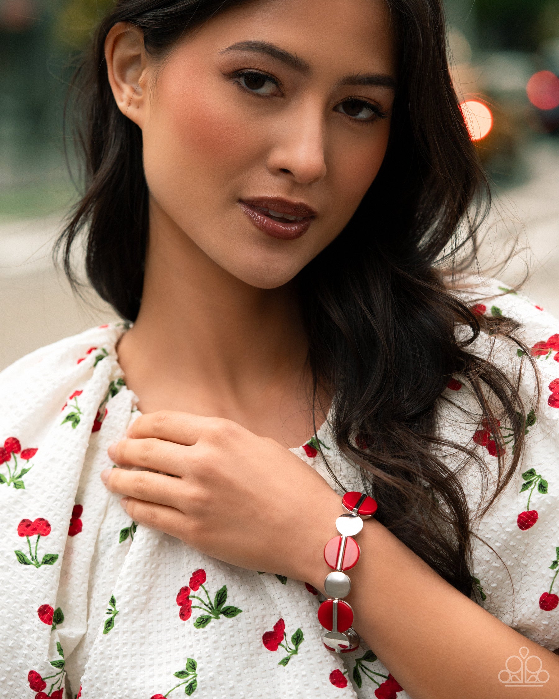 Woman wearing a white dress with red floral patterns and a bracelet outdoors.