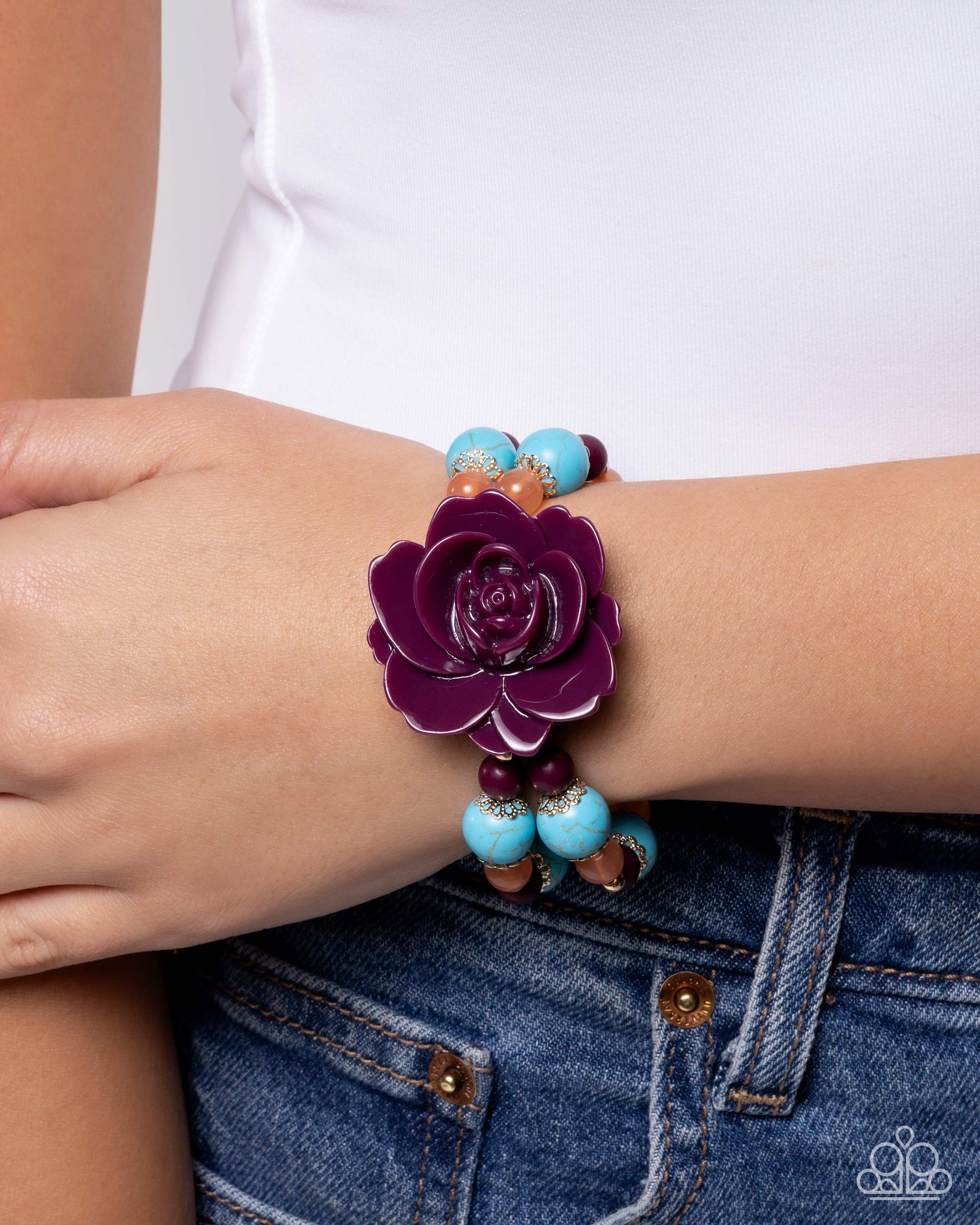 Bracelet with purple flower and turquoise beads on wrist against white shirt and blue jeans
