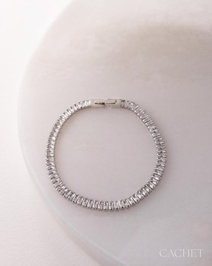 Silver bracelet with clear stones on a light pink background, featuring the brand 'Cachet'.