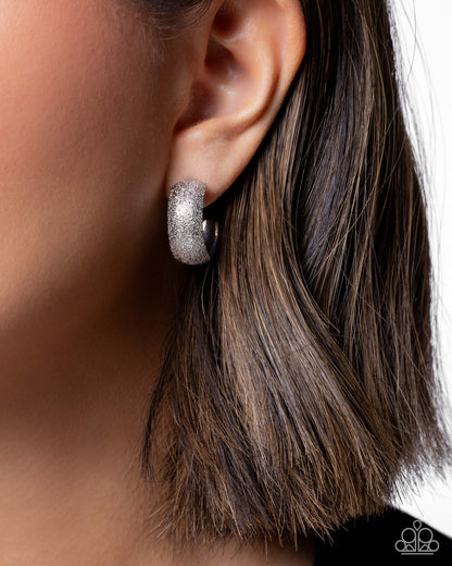 Silver hoop earring worn by a person with brown hair.