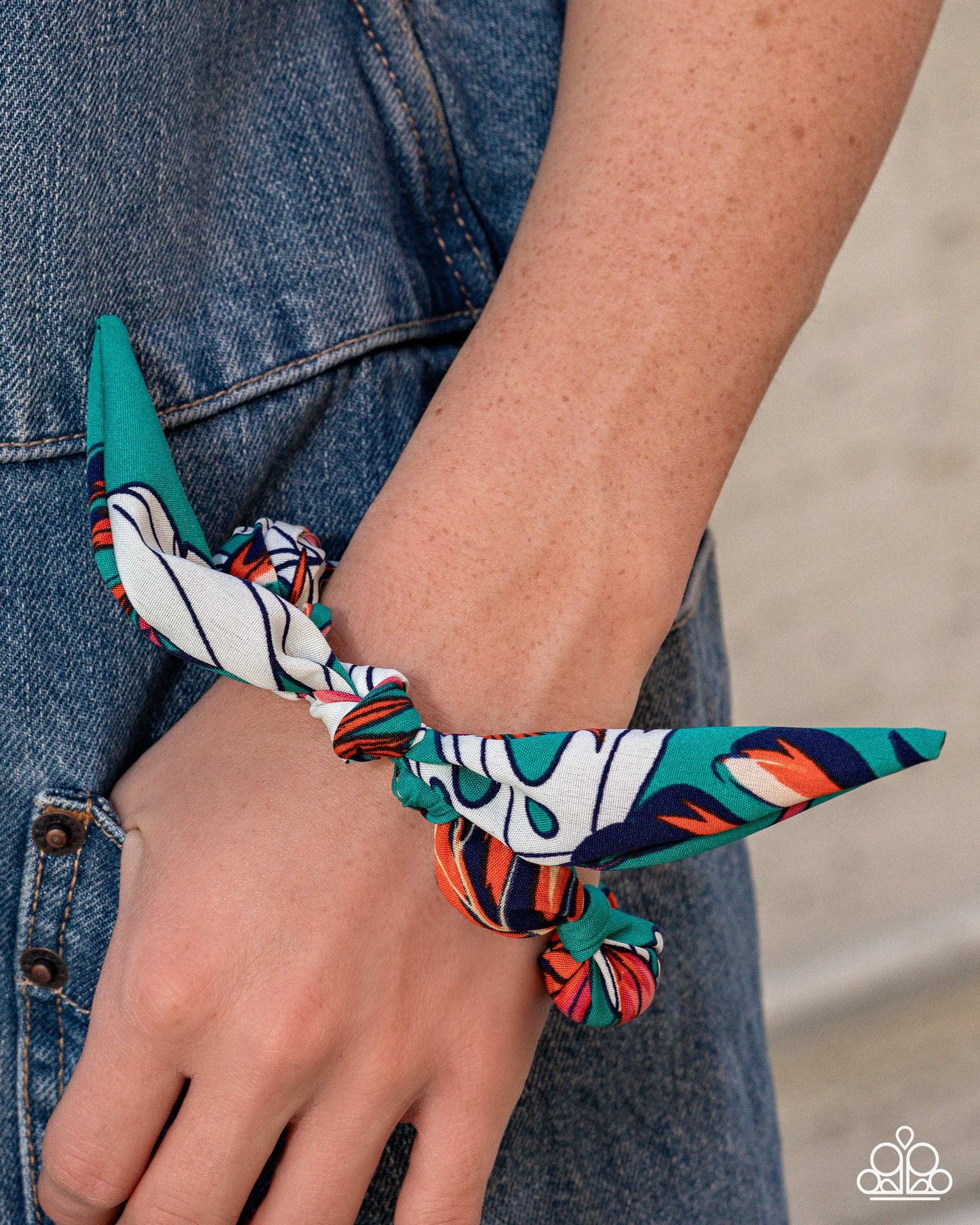 Multicolored patterned hair tie worn on a wrist with a denim background