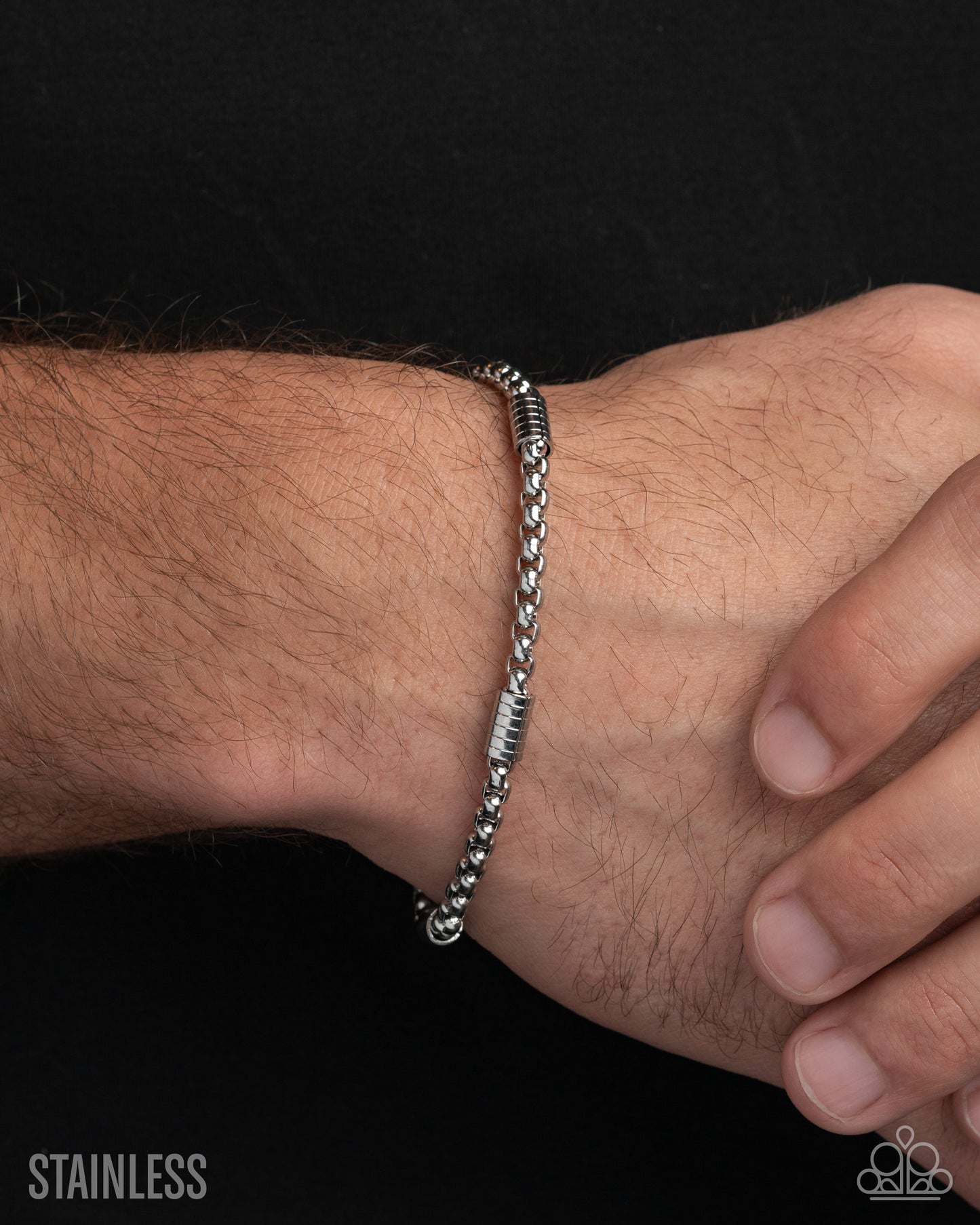 Silver bracelet on a wrist with a black background