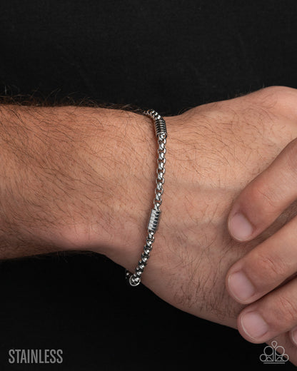 Silver bracelet on a wrist with a black background