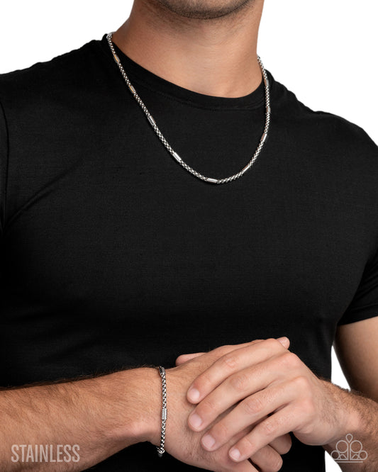 Person wearing a silver chain necklace and bracelet on a black shirt.